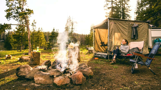 woman sitting next to tent and campfire