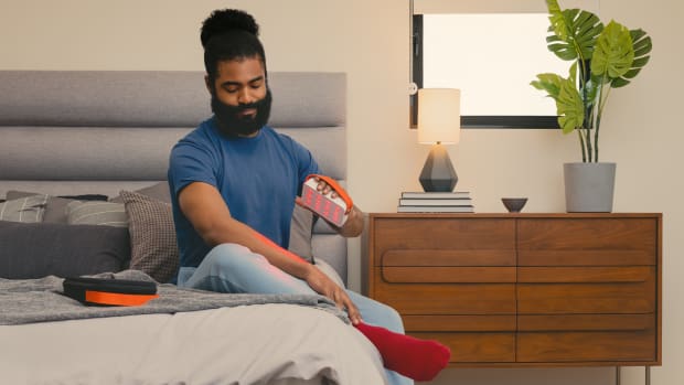 Here's why red light therapy benefits might help you beat seasonal affective disorder. Image of man siting on bed holding red light therapy tool.