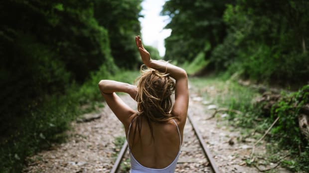 woman in a forest on train track with hands in hair and above head