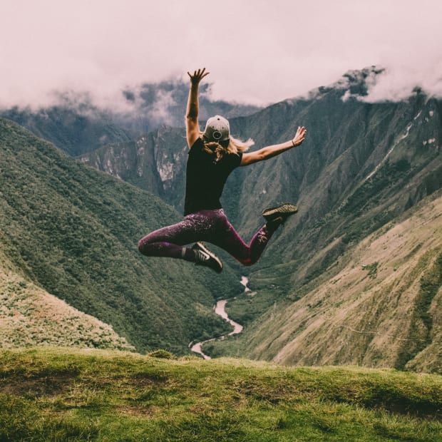woman leaping high over a beautiful view of the valley - ways to keep your mitochondria strong