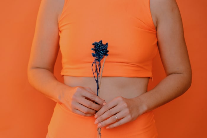 Woman wearing orange holding a flower in front of torso