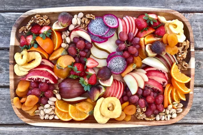Colorful fruit platter with dragonfruit, apple, strawberry, oranges, grapes, and walnuts.