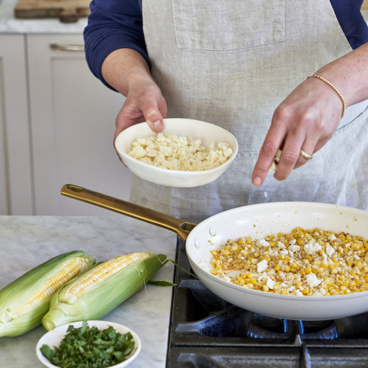 Making corn with fresh queso in a white ceramic nonstick pan.