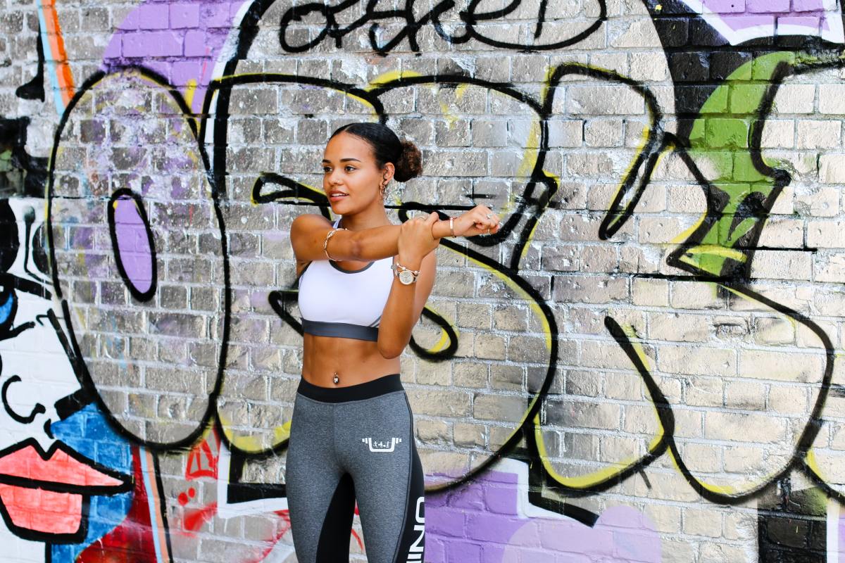 Woman in workout clothes stretches in front of graffiti wall.