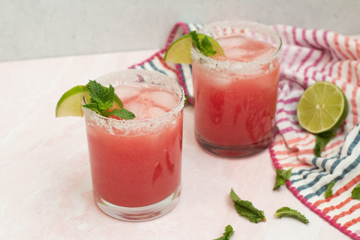 two watermelon margaritas with a striped towel and lime