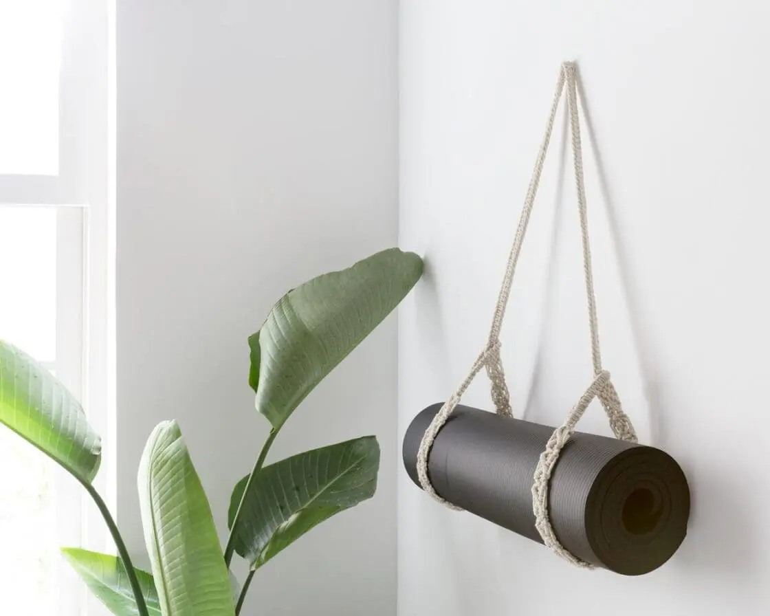 Black yoga mat suspended in macramé rope hanging with green plant leaves visible
