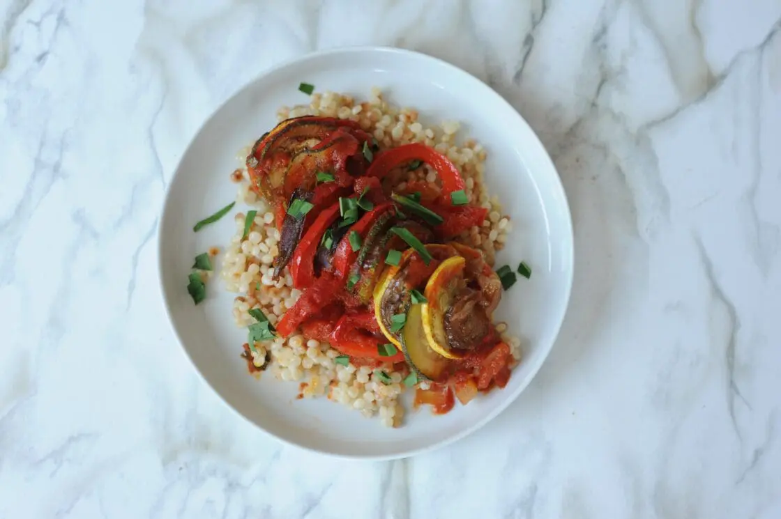 image of vegan ratatouille served on a white plate. This vegan ratatouille recipe is picnic-friendly and just the thing to take on the go al fresco.
