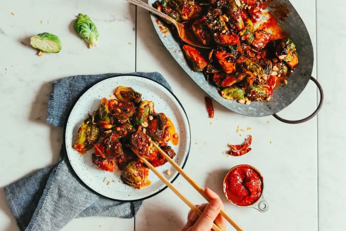 Roasted Brussels sprouts with red sauce and chopsticks on white plate