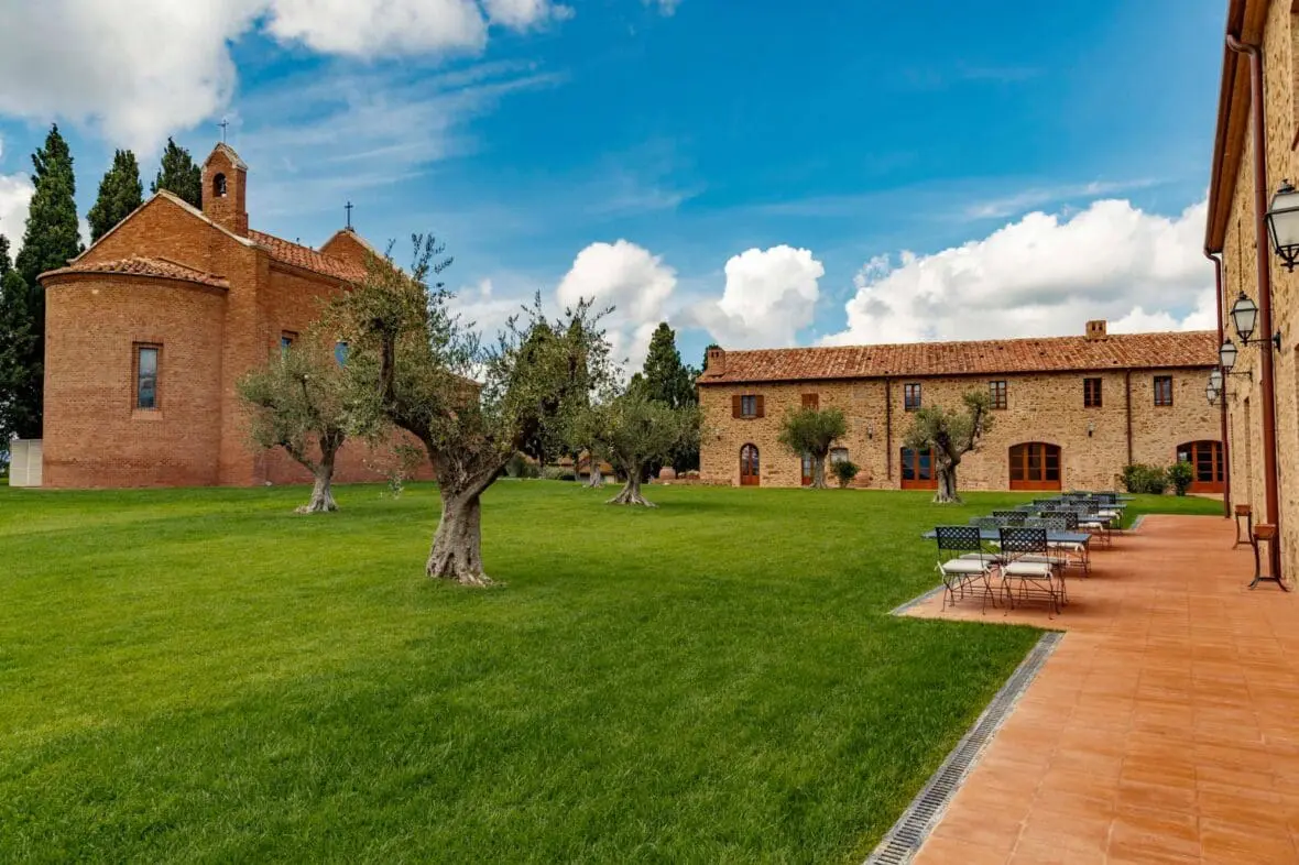 Tuscan wine estate courtyard with brick chapel, stone buildings, olive trees, and terracotta terrace