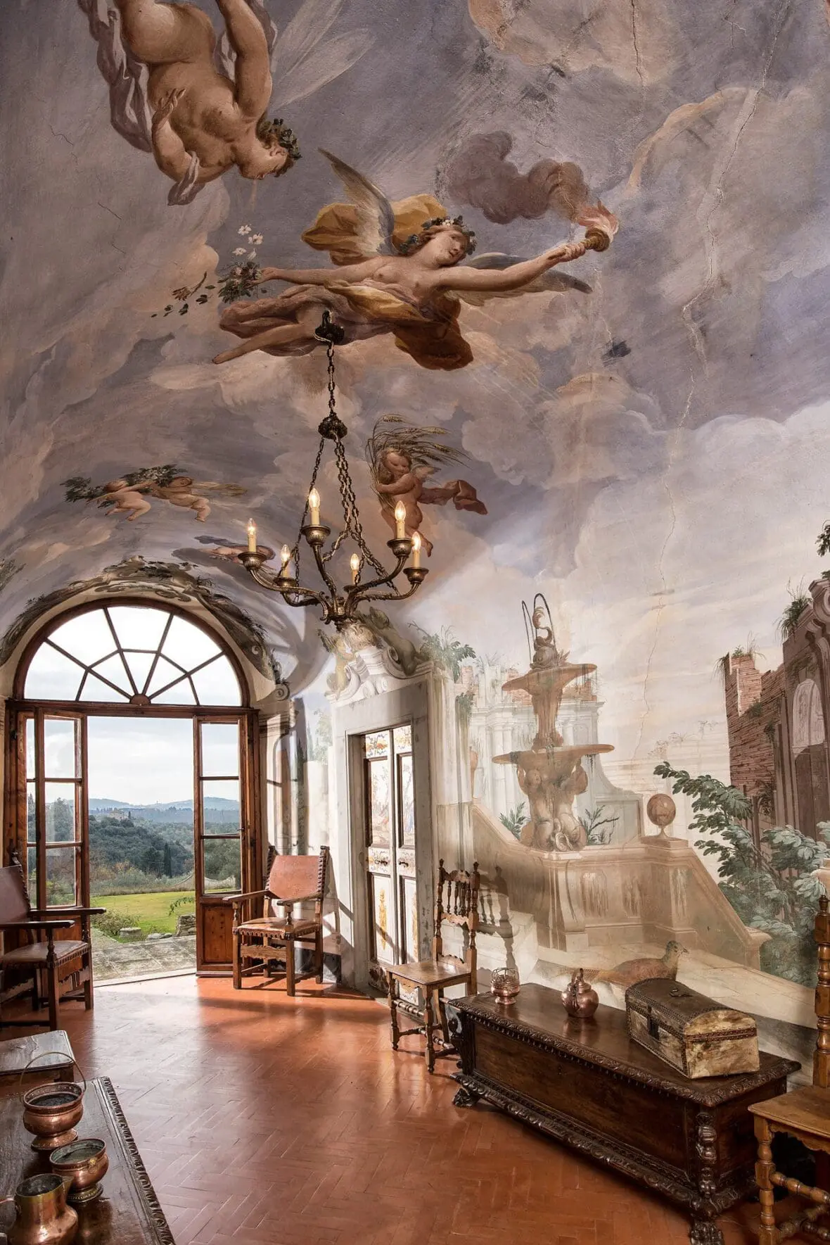 Ceiling fresco with cherubs and chandelier in Italian villa interior with arched window overlooking