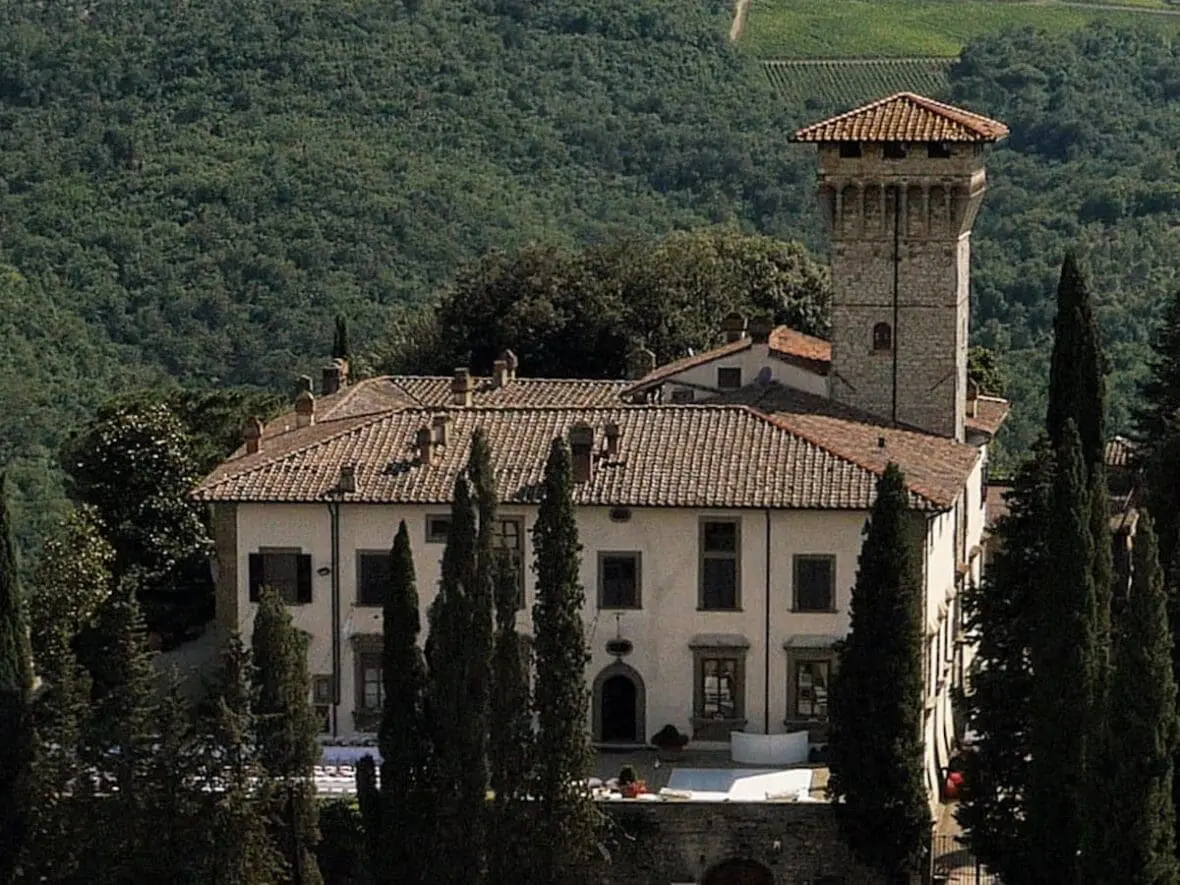 Italian villa with terracotta roof and bell tower surrounded by cypress trees and forested hills