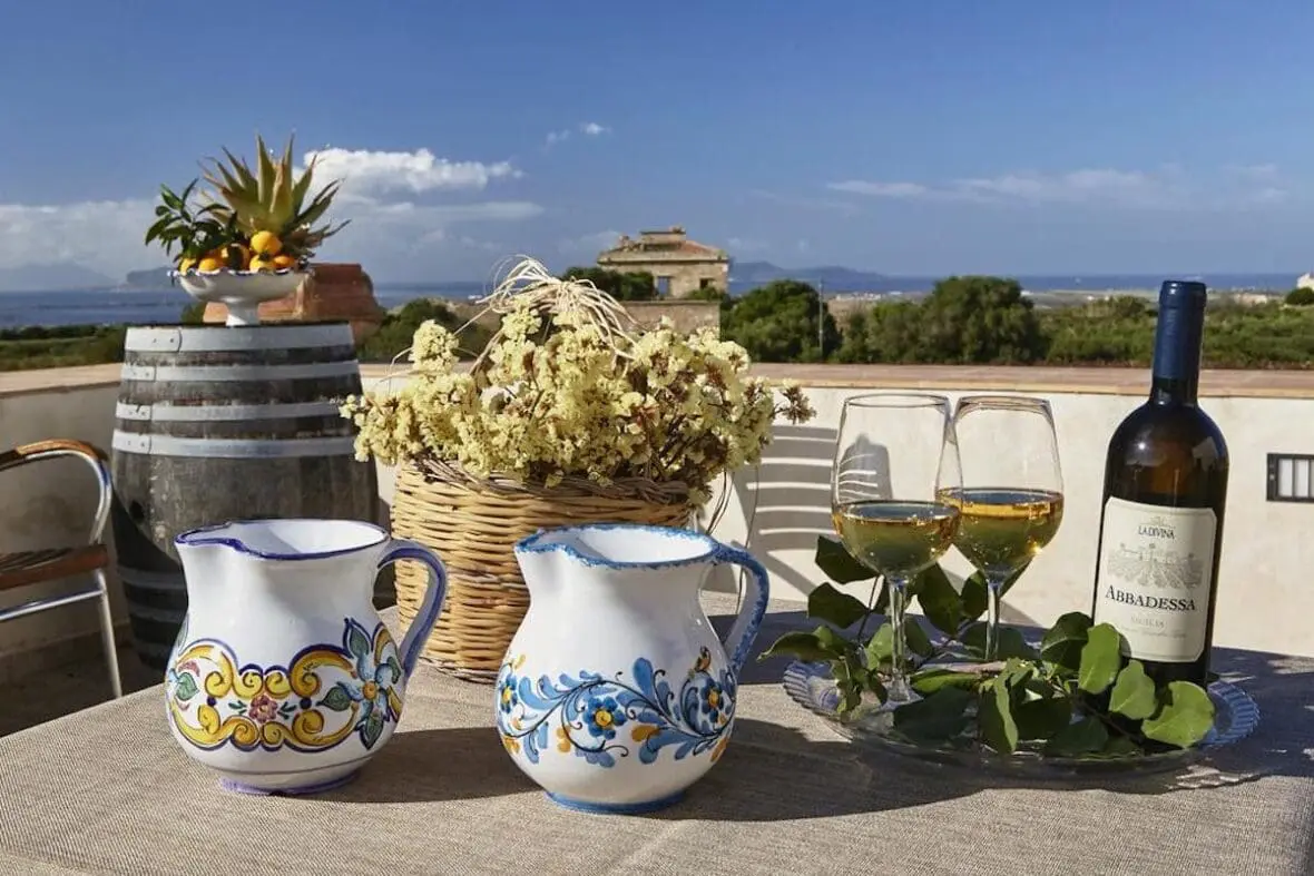 Italian wine estate terrace with white ceramic pitchers, wine glasses, and Abbadessa wine bottle