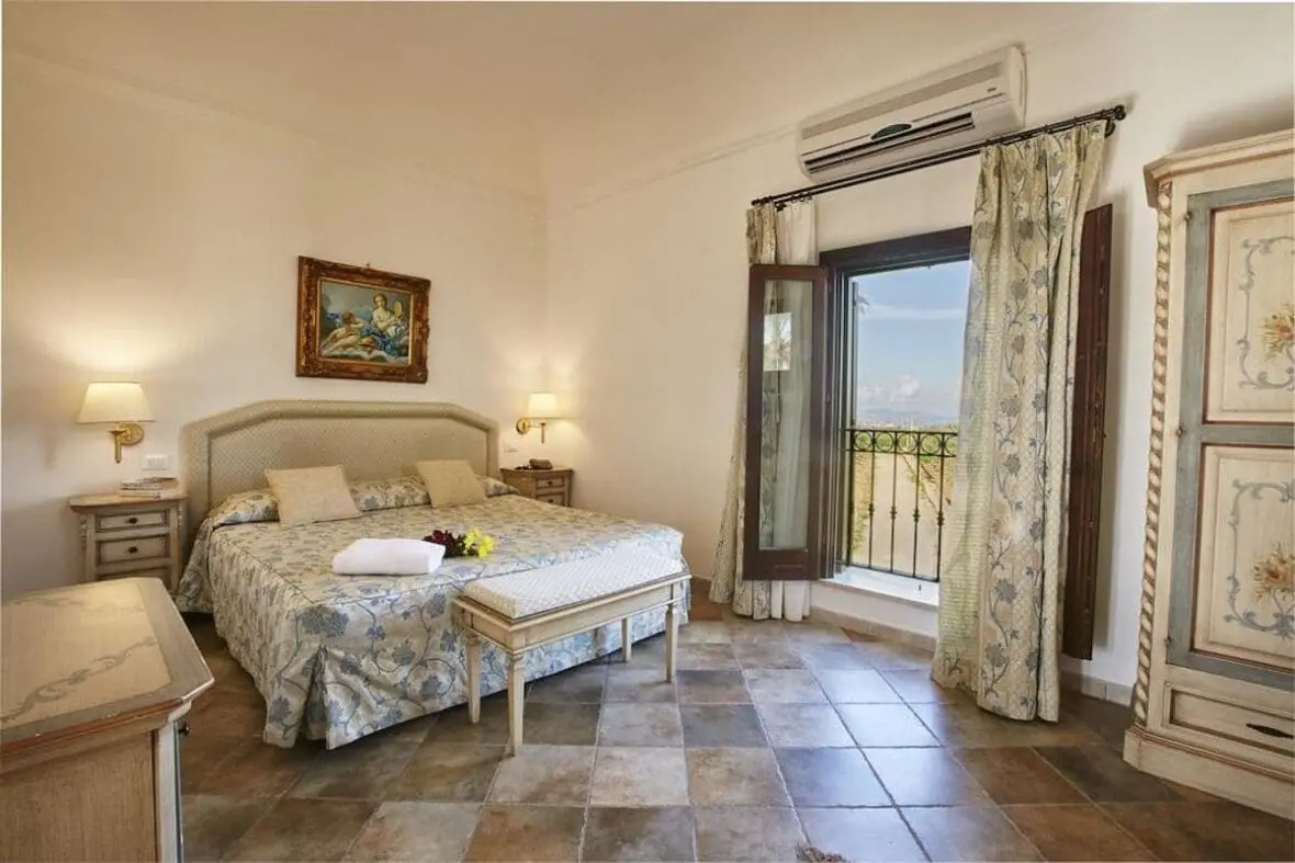 Elegant bedroom with blue floral bedding, terracotta tile floors, and balcony view at Italian wine