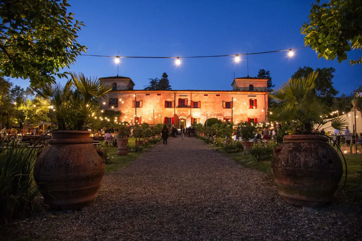 Italian villa illuminated at dusk with terracotta pots, string lights, and manicured gardens