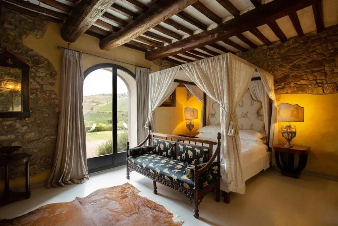 Luxurious bedroom with canopy bed, exposed wooden beams, and arched window overlooking Tuscan