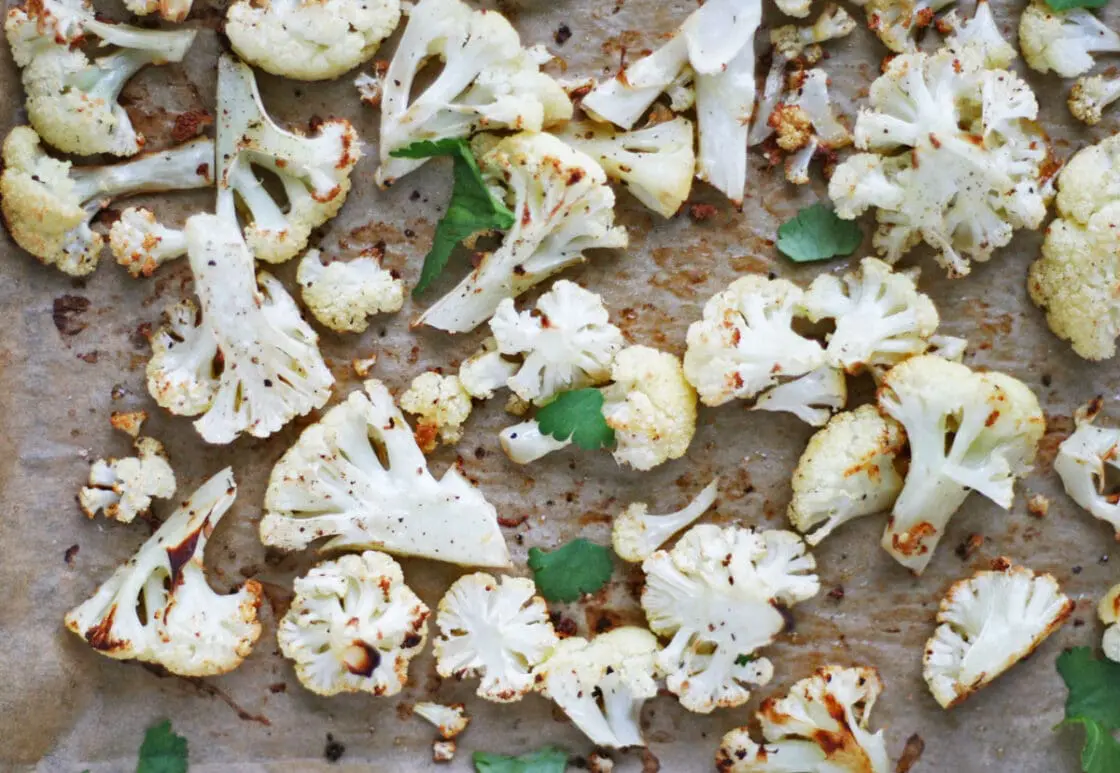 Roast cauliflower florets on a sheet pan with fresh parsley.