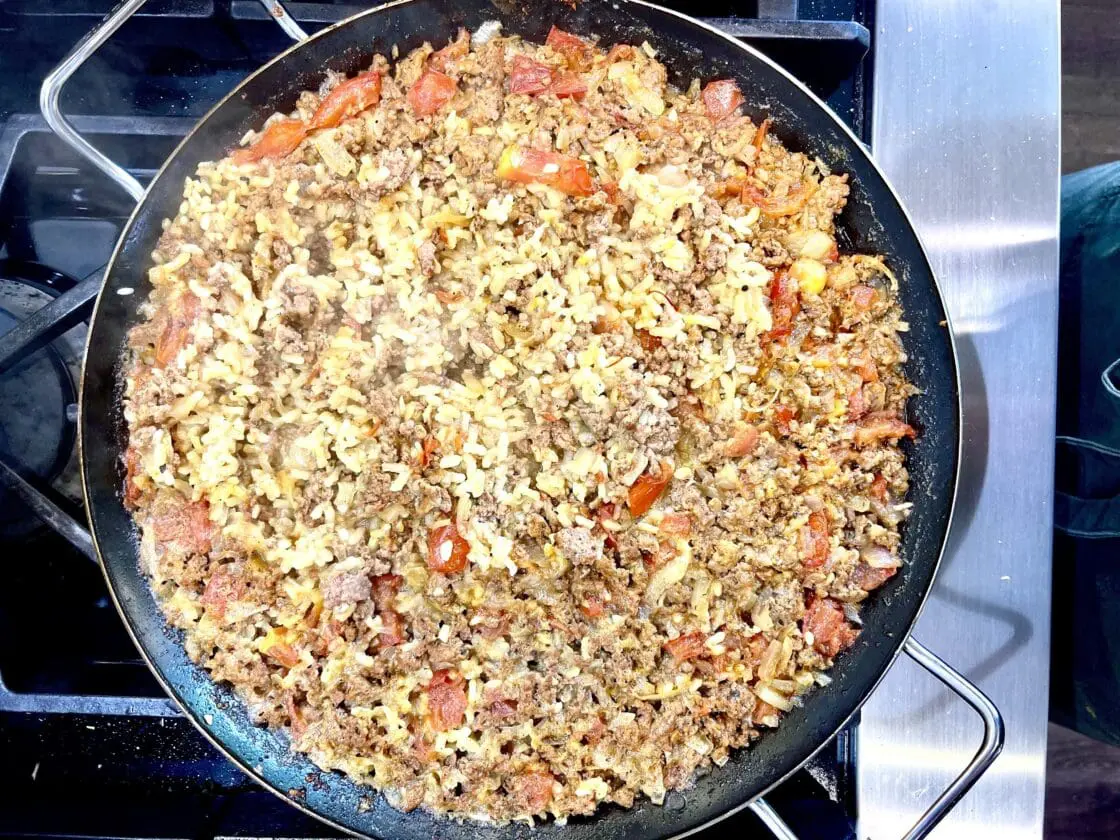 Paella rice and soffrito in pan on stove top.