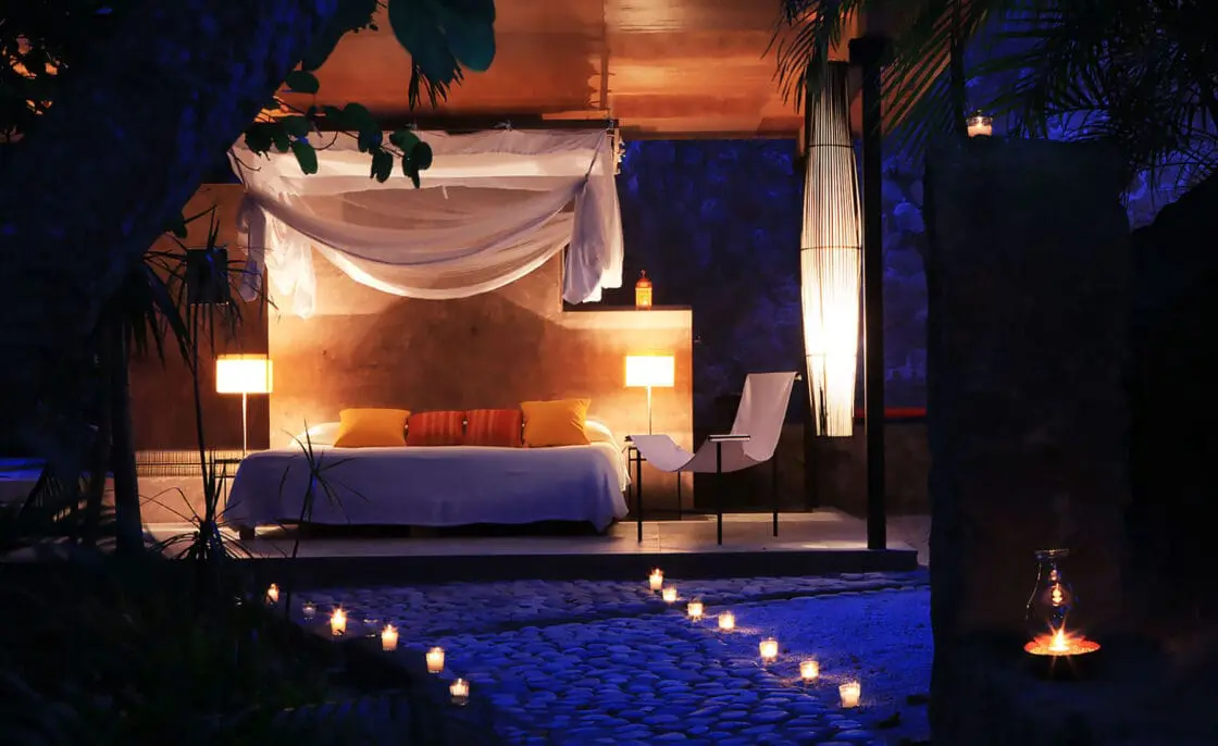 Luxurious beachfront bedroom at VERANA hotel with candlelit sand, draped canopy bed, and warm