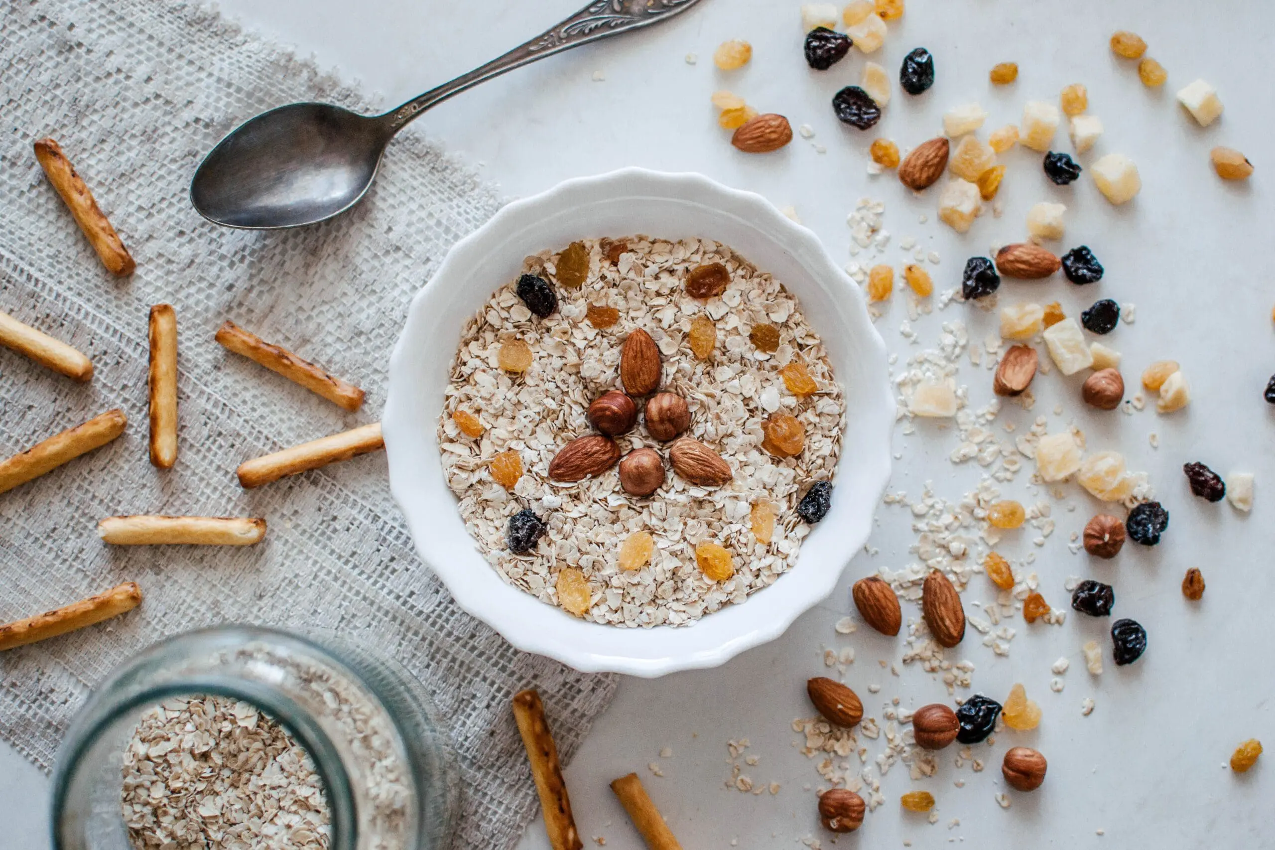 Bowl of oatmeal with almonds, raisins, and berries surrounded by nuts and dried fruit
