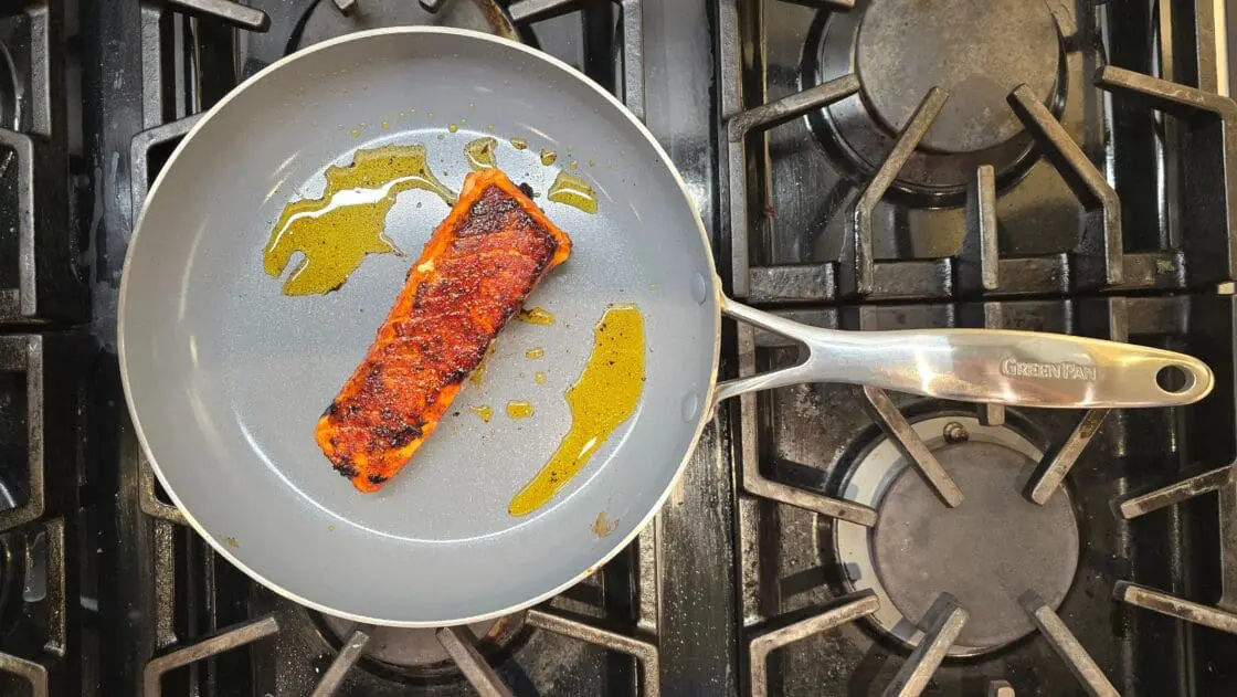 Image of a GreenPan Valencia Pro Stainless Steel frypan with a filet of salmon and a little olive oil on a gas range showing the nonstick properties that Laura Klein has maintained after years of greenpan review and testing.