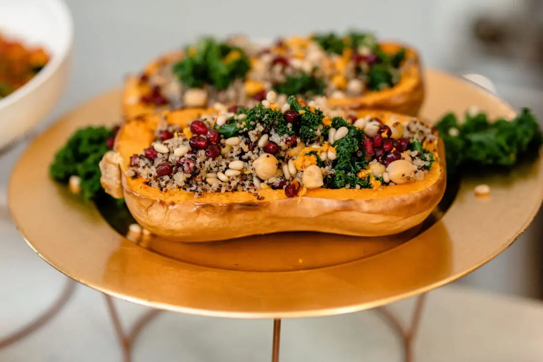 vegan stuffed butternut squash stuffed with quinoa and pine nuts served on a gold plate
