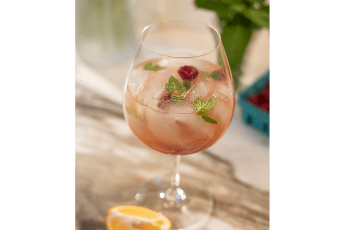 Image of white wine spritzer with kombuca in a pretty wine glass with raspberries and mint.