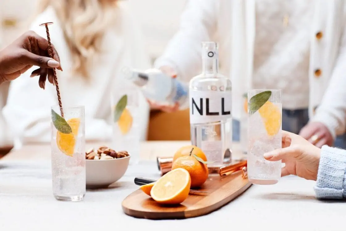 Image of New London Light non-alcoholic spirits served as easy mocktails with slices of lemon and a leaf of sage, with four women standing around the serving table.