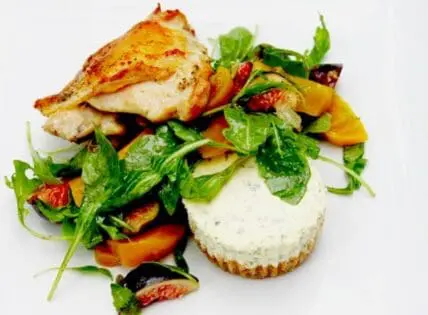 Plated dish with seared chicken breast, roasted vegetables, fresh arugula, and creamy white sauce