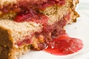Sliced peanut butter and jelly sandwich with red jam filling on white plate