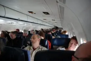 Crowded airplane cabin with passengers seated in rows of blue seats