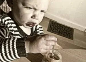 Toddler in striped sweater eating from a bowl with a spoon