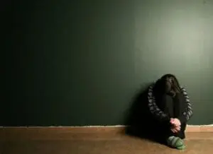 Woman sitting alone against wall with head down, appearing distressed or anxious