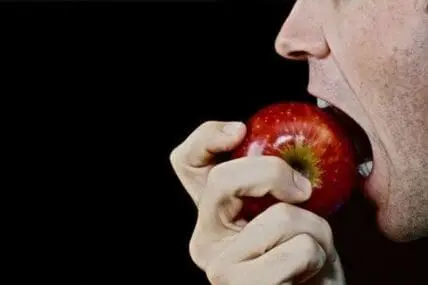 Man biting into a red apple against a black background