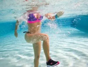Child running underwater in shallow ocean water wearing colorful swim gear
