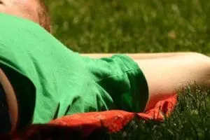 Person in green shirt lying on grass with red cloth