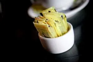 White ceramic bowl filled with yellow artificial sweetener packets on a dark surface