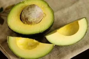 Halved and sliced avocado showing pit and creamy yellow-green flesh on neutral fabric