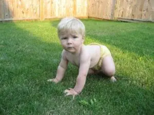 Toddler in yellow diaper crawling on grass in backyard