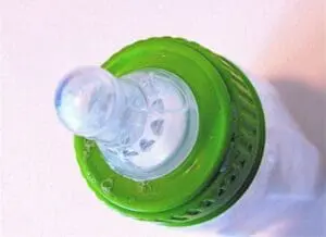 Top view of a green baby bottle with clear liquid and measurement markings inside