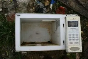 Discarded microwave with open door sitting on ground outdoors