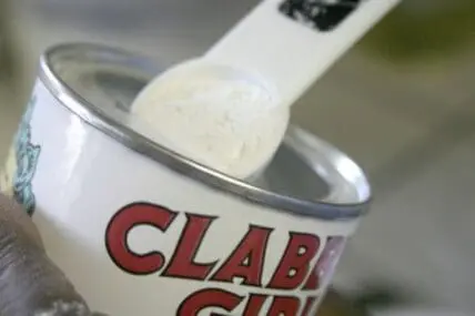 A measuring spoon scooping expired baking powder from a container