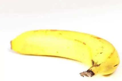 Single yellow banana with brown spots on white background