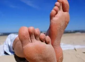 Bare feet relaxing on sandy beach with ocean and sky in background