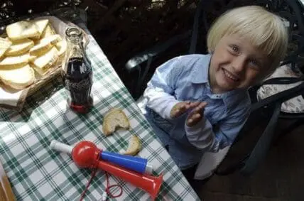 Young child enjoying a healthy picnic meal with bread, tomato, and cola