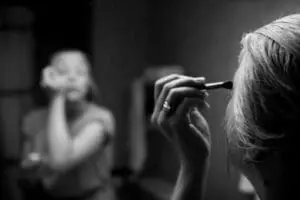 Woman applying makeup with a brush, looking in a mirror