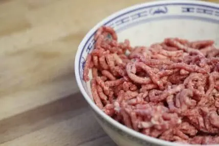 Ground beef in a ceramic bowl on a wooden surface