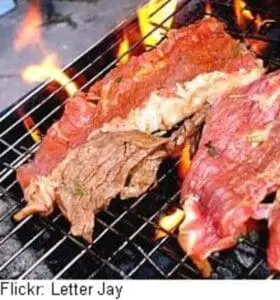 Various cuts of meat grilling over open flame on a barbecue grate