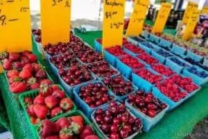 Fresh berries displayed in colorful containers at a farmers market stall with yellow price signs