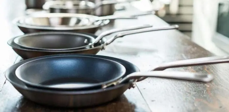 Image of a line of Made In frypans lined up and stacked by twos on a wood countertop, the front stack of two is in focus, the rest are out of focus. This brand is a good alternative to the best ceramic cookware brands.