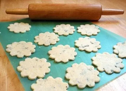 Sage-infused flower-shaped cookies on a turquoise mat with a wooden rolling pin